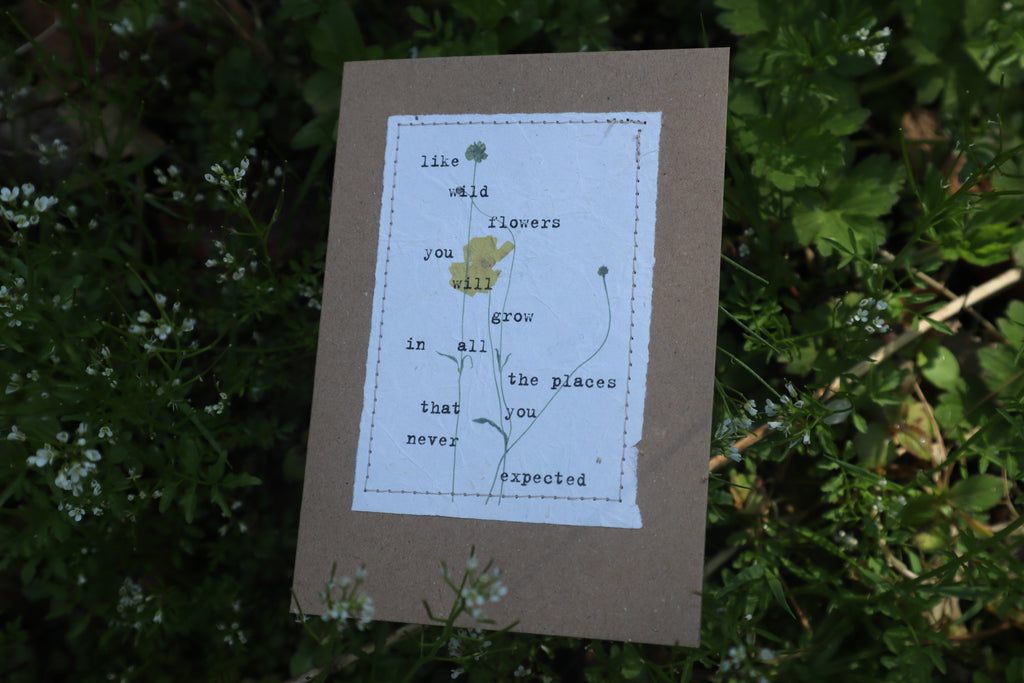 alt="handmade postive affirmation card by abby monroe resting on a bed of wildflowers. card available from bramble and fox uk hygge shop"