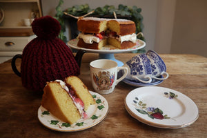 alt="afternoon tea scene with mismatched china, teapot and victoria sponge cake. Available from Bramble and Fox UK hygge and cottagecore shop."