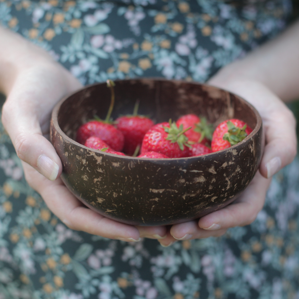 alt="woman's hands holding a Jungle Culture  coconut shell bowl filled with strawberries. Available from Bramble and Fox UK hygge cottagecore shop"