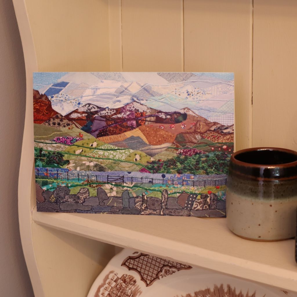 alt="snowdon patchwork art card by Josie Russell, next to a handmade mug. Available from Bramble and Fox UK hygge gift shop"