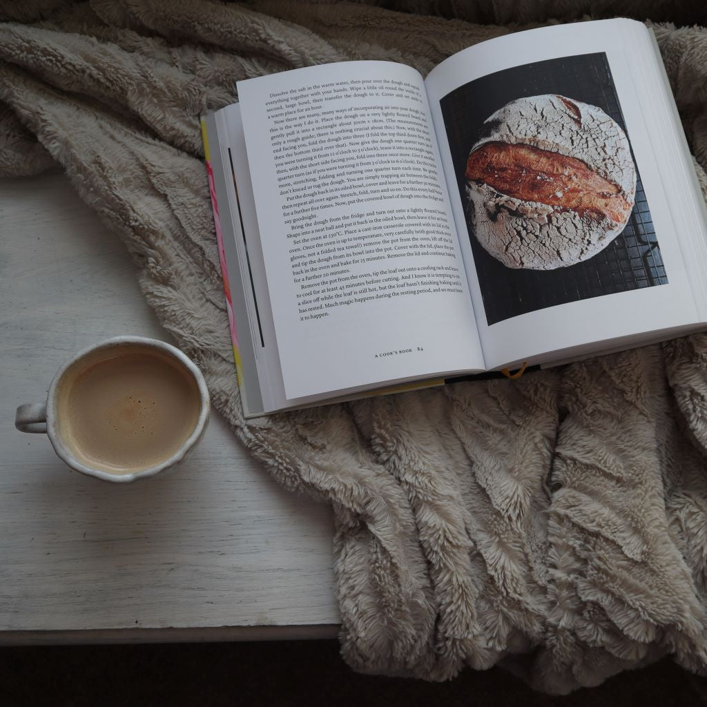 alt="Open copy of Nigel Slater's A Cook's Book with picture of sourdough loaf visible. Handmade cup nearby. Available from Bramble and Fox UK cosy homewares."