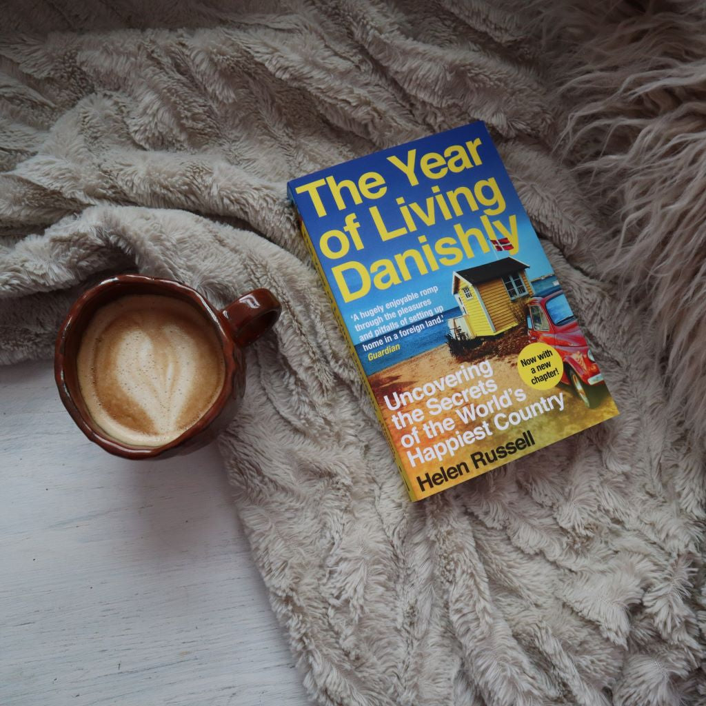 alt="The Year of Living Danishly book next to a handmade cup with latte art and a scandi style blanket. Available from Bramble and Fox UK hygge homeware shop"
