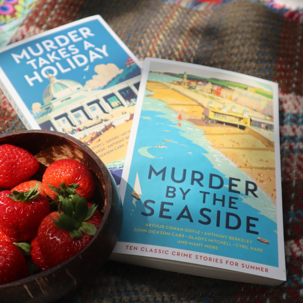 alt="close up of Murder By The Seaside Profile Books crime collection. A copy of Murder Takes a Holiday is in the background along with a tartan picnic blanket and a coconut shell bowl containing strawberries. All available from Bramble and Fox UK hygge cottagecore homewares"