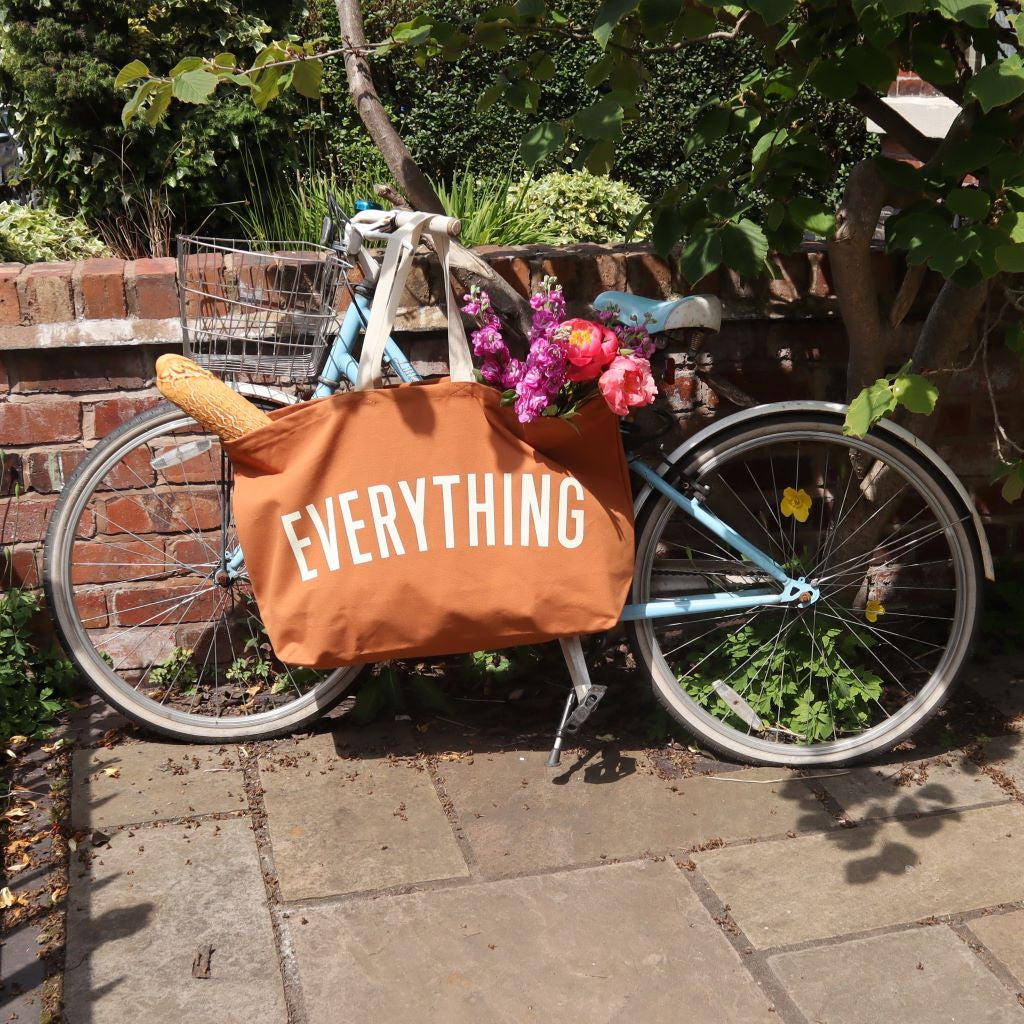 alt="pale blue Pendleton bike featuring an oversized canvas tote bag emblazoned with the word EVERYTHING. A baguette and a bunch of flowers are peeking out of the top of the bag. Made by Alphabet Bags. Available from Bramble and Fox UK hygge gifts and homewares"
