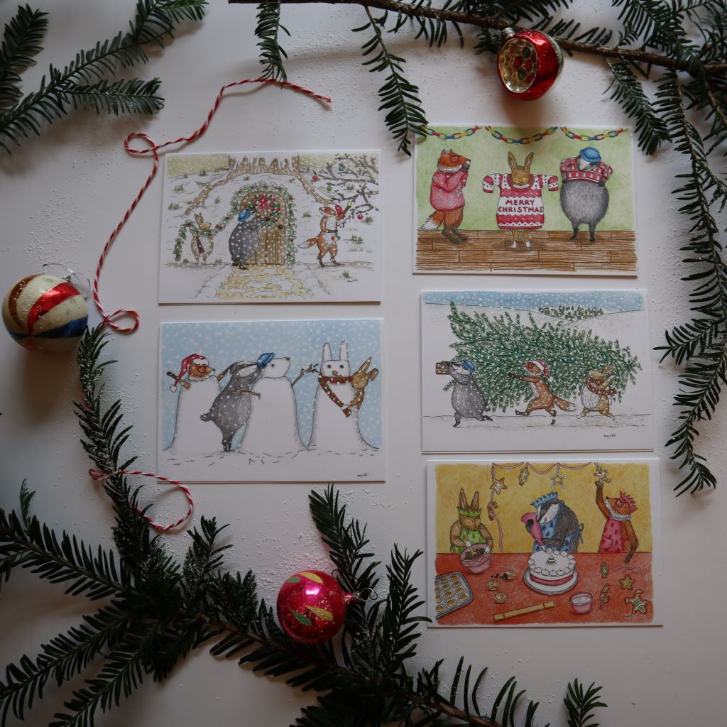 alt=" Festive flatlay of woodland friends christmas cards by kerry dilks. Join badger, fox and rabbit as they celebrate christmas. Cosy illustrations in the style of raymond briggs, janet ahlberg and beatrix potter. Available from Bramble and Fox UK hygge shop"
