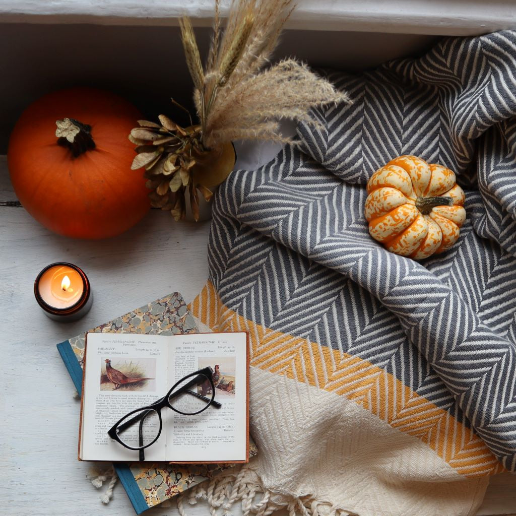 alt="cosy flatlay featuring Ochre & Flax soy candle, pumpkins, and a cream, grey and mustard scandi blanket. An open copy of The Observer's Book of Birds and a marbled paper journal are in the foreground. All hygge home decor is available from Bramble and Fox UK hygge interiors shop."