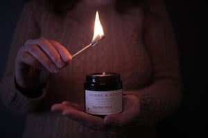 alt="hands holding lit match and Ochre and Flax Exuberance pure soy wax candle. Available from Bramble and Fox UK hygge gifts and homewares"
