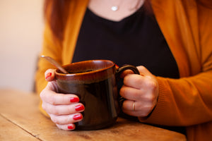 alt="kiln craft drip glaze vintage mug in earthy colours being cradled in hands by bramble and fox uk hygge shop"