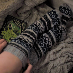 alt+"woman's legs in long fair isle woollen socks. A copy of The Forager's Calendar book is next to her on a blanket. Available from Bramble & Fox UK hygge gifts and homewares"