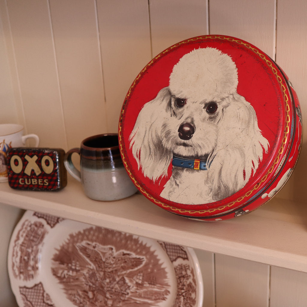 alt="vintage peek and frean poodle biscuit tin displayed on dresser shelf. Available from Bramble and Fox UK hygge shop."
