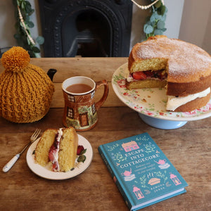 alt="price kensington cottage mug in an afternoon tea scene with tea, cake and the book Escape into Cottagecore. Available from Bramble and Fox UK cottagecore homeware shop"