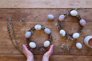 alt="flatlay featuring woman's hands holding rustic spring wreaths featuring handpainted eggs. cruelty free feathers and pussy willow. Available from Bramble and Fox UK hygge and cottagecore homewares"