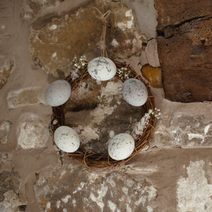 alt="rustic easter wreath hanging on a rough stone cottage wall next to a rustic beam. Wreath available from Bramble and Fox UK hygge homewares"